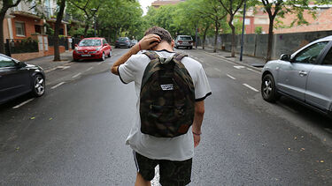 A shot of a male student from behind walking alone down a road.