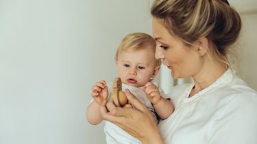 A Mother holding a child, showing them a wooden toy