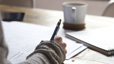 Person sat at a desk with a pen and cup of tea