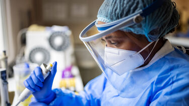 Researcher working in a biochemist laboratory. Female doctor wearing full PPE suit, face mask, and face shield working with pathogen samples in lab.