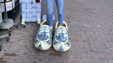girl sticking up both thumbs wearing massive Dutch clogs. You only see her ankles and the clogs