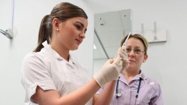 Apprentice student holding a syringe under the supervision of an NHS worker.