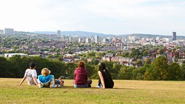 A scenic shot of some individuals sat on a green space overlooking the city