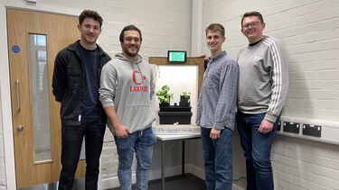Photograph of Alex and other group members standing next to their final year project, a climate control system to grow plants inside a box
