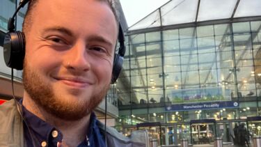 Jacob Waters holding a microphone outside of Manchester Piccadilly train station