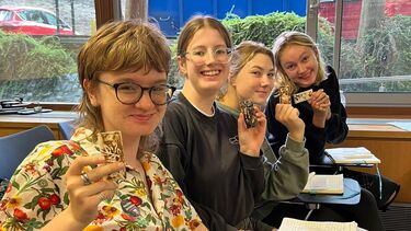 4 student holding up a small tile to the camera. 