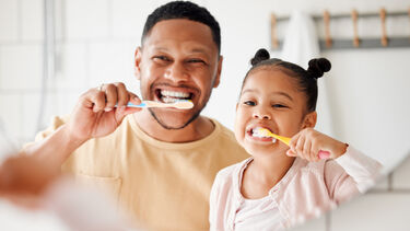 A father and daughter look in the mirror as they brush their teeth