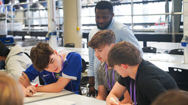 Three year 12 students working at a table as a an academic observes