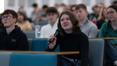 Student with mic asking a question with other students in the background