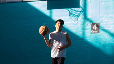 A man in a white tank top holding a basketball in a gymnasium