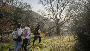 Three students wearing backpacks walking in the countryside in autumn