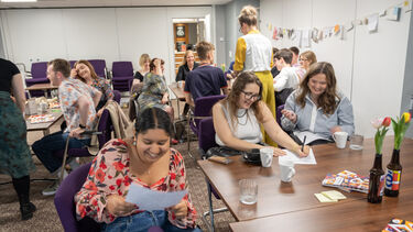 group of people smiling around tables busy doing some task: question bingo