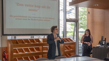 a young woman with some cards in her hand ready to deliver a presentation while Filip De Ceuster introduces the speaker. she will talk about the Dutch habit of 'wall snacking' 