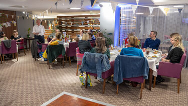 people sitting around dinner tables with one person Michael Perraudin standing and speaking. Informal setting