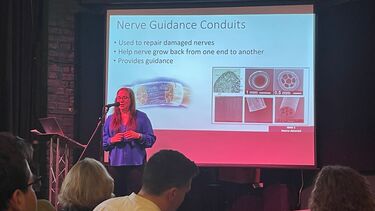 Dr Caroline Taylor standing in front of a projected screen and speaking into a microphone