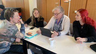 Paulien Cornelisse listening intendly to a story read by one of the participants. Two more students are sat at the table and are listening