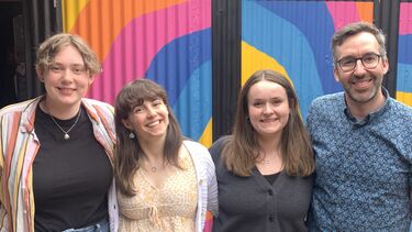 Four people standing next to each other against a colourful background, smiling