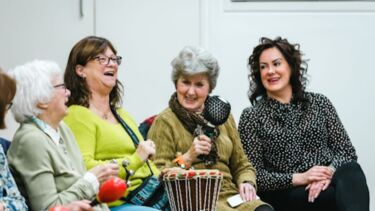 Four seated people are laughing as they play musical instruments