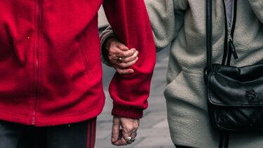 Torsos of two people walking - one person links arms with the other for support