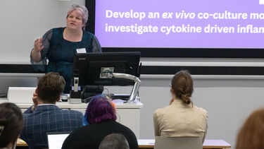A woman with short grey hair stood behind a lectern speaking to an audience in a lecture theatre
