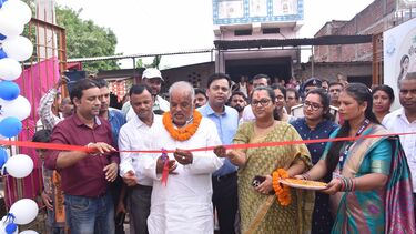 Honourable Minister for Rural Development, Shri Shravan Kumar cutting the ribbon to officially open the market. A crowd is stood behind and to the side of him.
