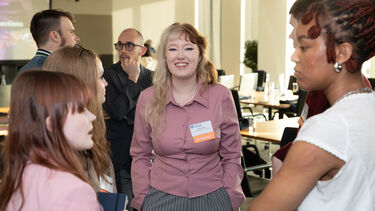 A group of students and alumni standing around chatting informally in a conference space
