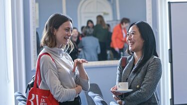 2 people stand talking at an event