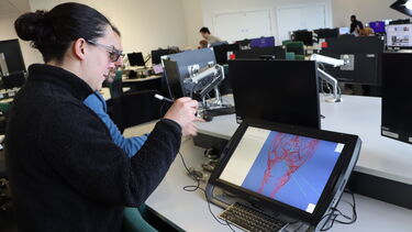 A woman wearing glasses with dark hair tied in a bun is looking at patient anatomy on a virtual reality tablet.