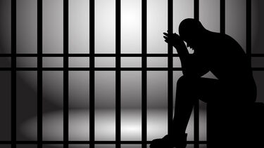 person sitting behind prison bars