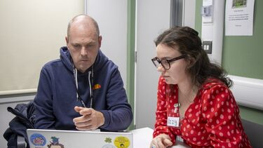 Two people sitting at a desk, looking at a laptop.