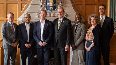 A group of seven colleagues from the Universities of Alberta and Sheffield stand in a row in a room, with a University of Sheffield crest behind them, and smile towards the camera.