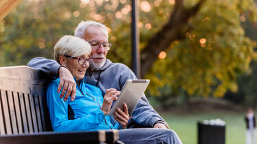 Two people sitting on a bench looking at an iPad