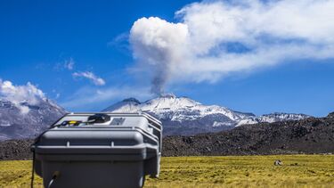 Some monitoring equipment pointing at a volcano with steam coming from its peak.