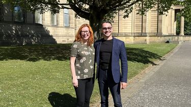 Sally and Karzan stand in Western Park in front of the museum and a tree