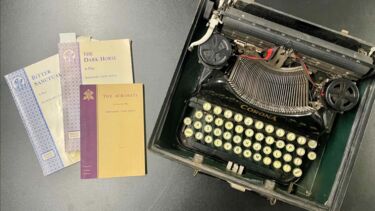 A typewriter with three paper books beside it