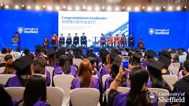 A photo from the back of the hall looking over student heads at the stage