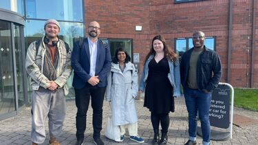 Five people stand outside a building, smiling at the camera 