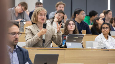 A woman sitting in a lecture theatre holding a microphone asking a question