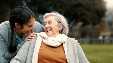 A young woman with an elderly woman smiling in a park.