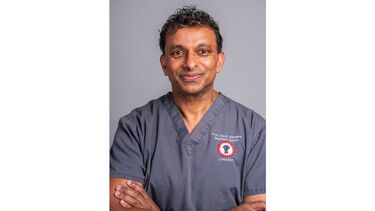 A man smiling with his arms crossed in scrubs.