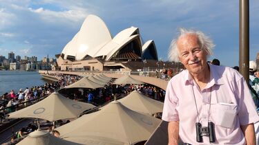A man smiling while standing in front of the Sydney Opera House