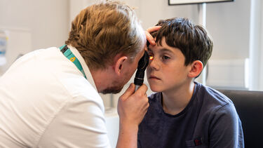 A male student uses equipment to look into a young patient's eye