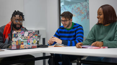Postgraduate students learning in a small group around a table. One has a laptop.
