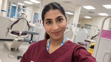Iram is in a dental teaching suite. She has dark hair which is tied back, and is wearing maroon scrubs.
