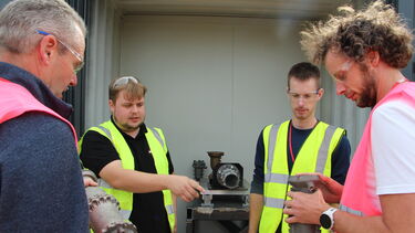 Four men in high visibility vests examine a piece of machinery 