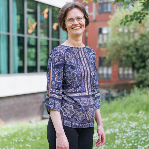 Profile picture of Rosanna stands on a grass bank with a building behind her 