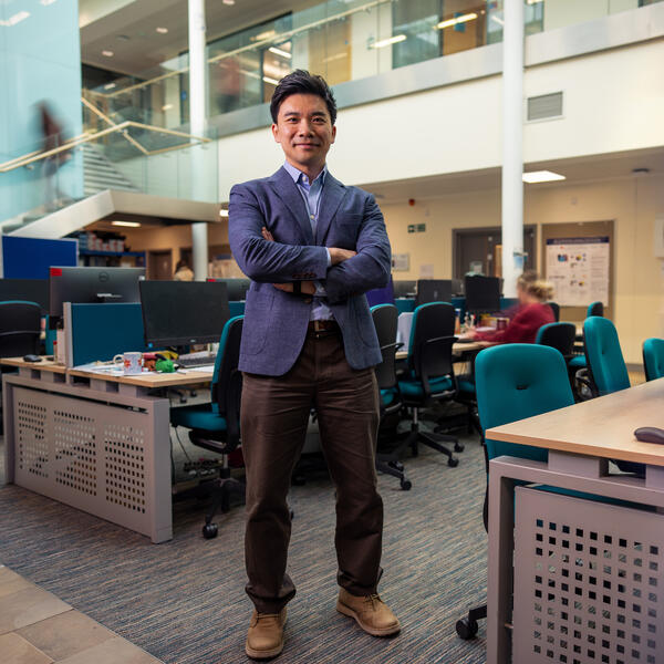Profile picture of Dr Leslie Ing stands arms crossed in a busy office space