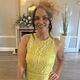 Becky wears a yellow dress and a fascinator. Her hair is dark brown/black and styled for a formal event.