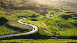 a road through the green hills of the peaks