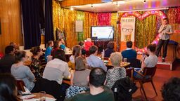 An audience watches a presenter on stage at a Pint of Science event.